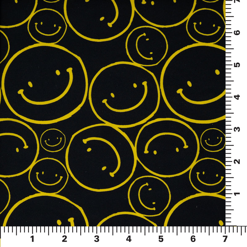 Flat sample shot of All Smiles Printed Spandex on a 7"x'7" ruler for pattern sizing. The print is of vibrant yellow smiley faces of various sizes on a black background.