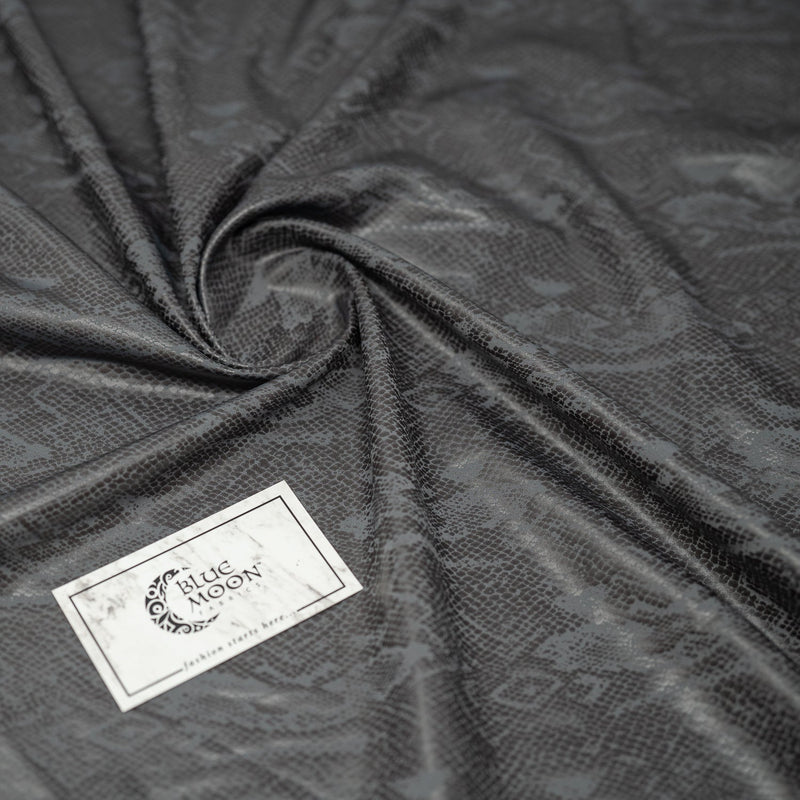 A swirled piece of Medusa Snake Skin Foil Printed Spandex in the color Grey with Blue Moon Fabrics logo