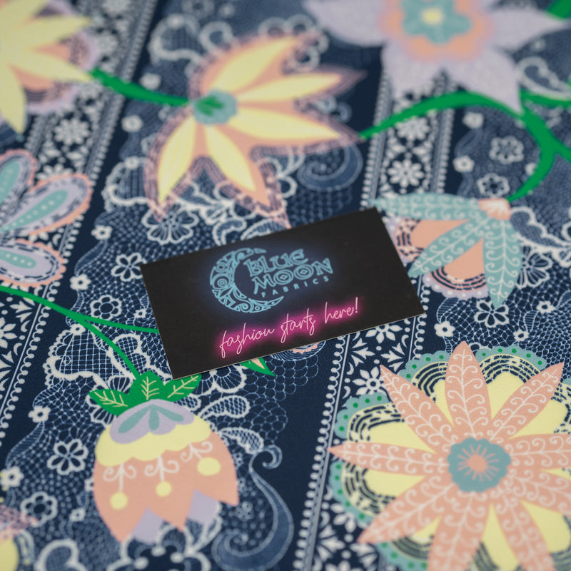 A flat sample of Chantilly Floral Lace Printed Spandex with a Blue Moon Fabrics standard size business card laid on top of the print for pattern sizing.