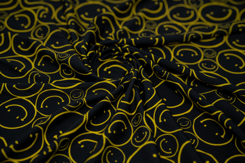 Swirled sample shot of All Smiles Printed Spandex. The print is of vibrant yellow smiley faces of various sizes on a black background.