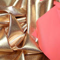 A crumpled piece of Alloy Foiled Spandex with rose gold foil on neon coral spandex.