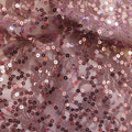 A swirled sample of charlize stretch lace sequin in the color mauve-orchid.