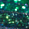 A folded sample of cosmic x spandex sequin in the color green-black available at blue moon fabrics.