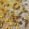 A flat sample of cottage garden stretch lace sequin in the color gold available at blue moon fabrics.