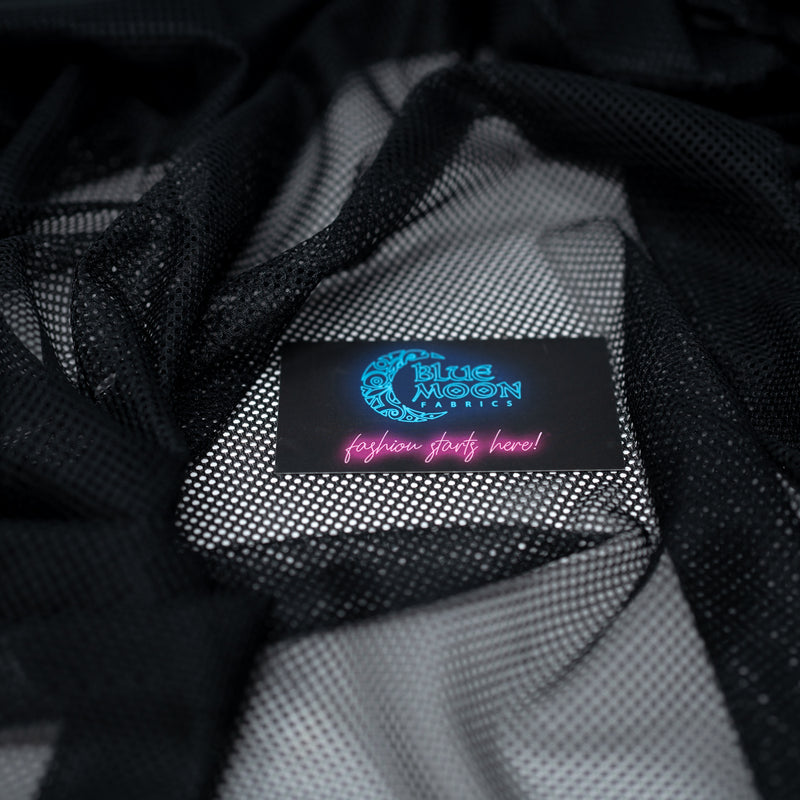 A crumpled piece of Polyester Mesh Tricot Boardshort and Swim Trunk Lining in the color Black with a Blue Moon Fabrics standard size business card laid on top of the print for pattern sizing.