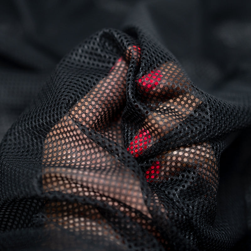 Hands playing with a sample of Polyester Mesh Tricot Boardshort and Swim Trunk Lining in the color Black