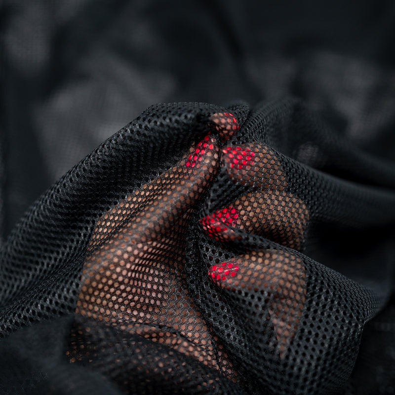 Hands playing with a sample of Polyester Mesh Tricot Boardshort and Swim Trunk Lining in the color Black