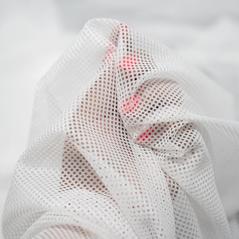 Hands playing with a sample of Polyester Mesh Tricot Boardshort and Swim Trunk Lining in the color White