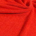 A swirled piece of crinkle polyester spandex jacquard fabric in the color poppy red.