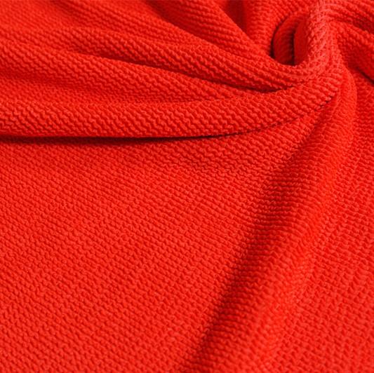 A swirled piece of crinkle polyester spandex jacquard fabric in the color poppy red.
