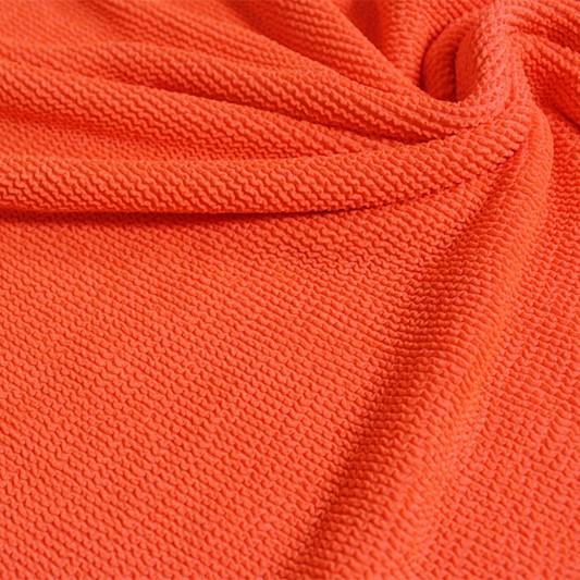 A swirled piece of crinkle polyester spandex jacquard fabric in the color vivid glow.