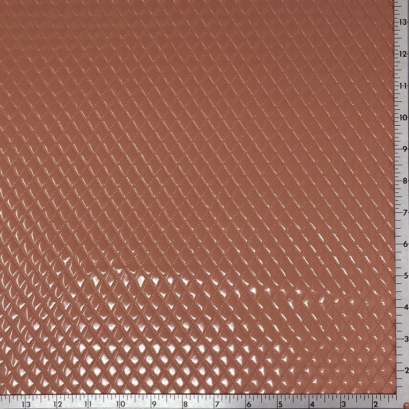 A sample of quilted hipster polyurethane coated spandex in the color light copper with a ruler for scale.