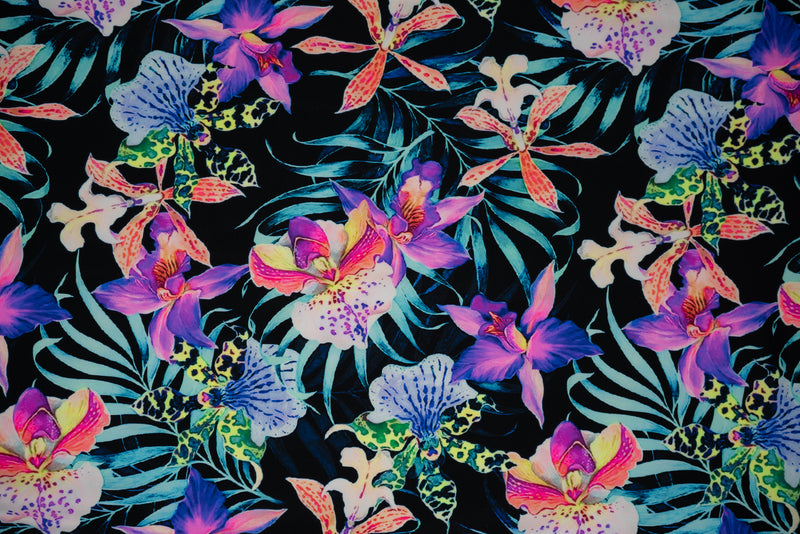 Flat sample of Irises and Palm Fronds Printed Spandex Fabric. The print is of vibrant colored Irises and other exotic flowers over bright light blue fronds on a black background.