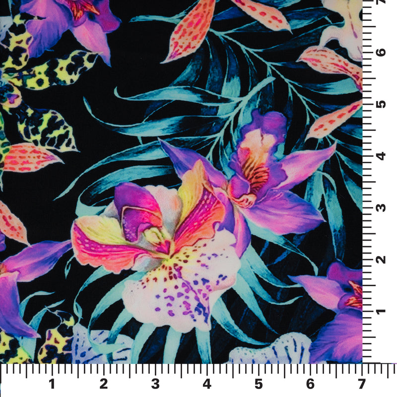 Flat sample of Irises and Palm Fronds Printed Spandex Fabric on a 7"x7" ruler for pattern scale. The print is of vibrant colored Irises and other exotic flowers over bright light blue fronds on a black background.