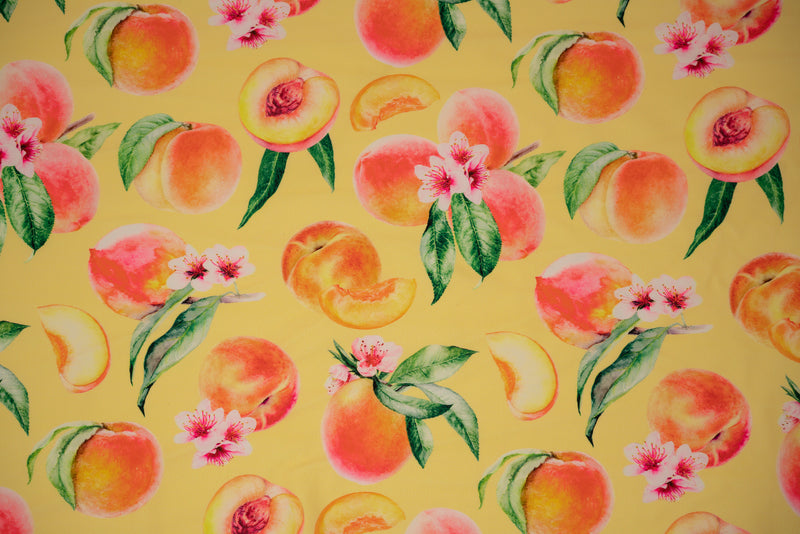 Flat sample shot of It's All Peachy Printed Spandex Fabric. The print is of whole peach clusters with pink peach blossoms and green leaves, whole individual peaches with peach slices and peach halves on a yellow toned background.  