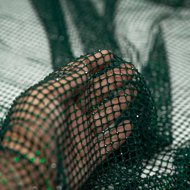 A hand pulling on a sample of Enigma Diamond Fishnet in the color Hunter-Green-Green