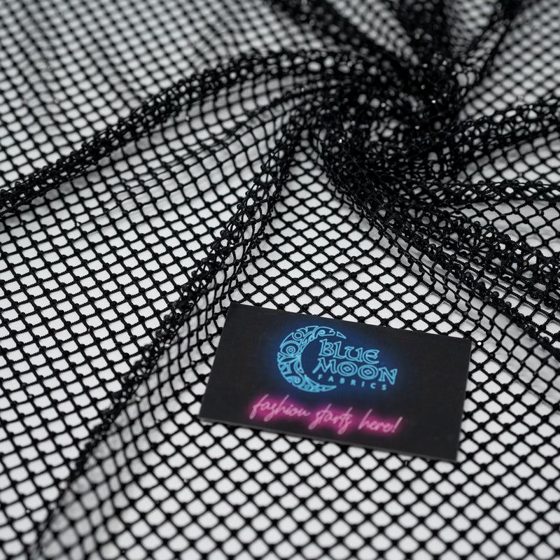 A swirled piece of Enigma Diamond Fishnet in the color Black with a Blue Moon Fabrics standard size business card laid on top of the print for pattern sizing.