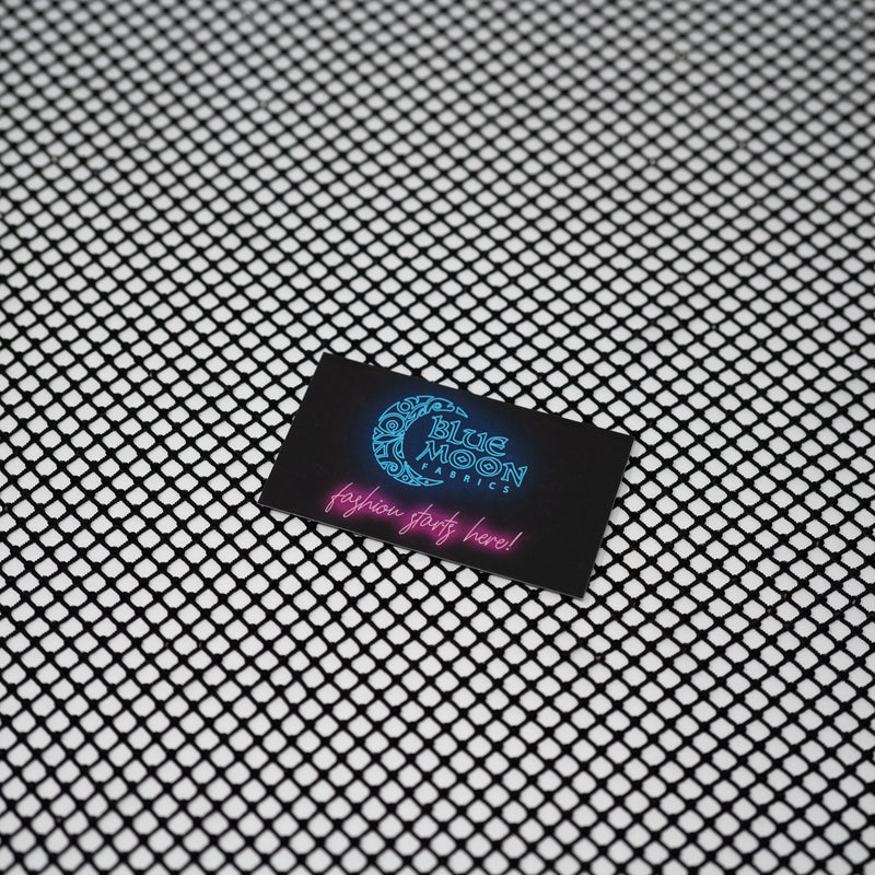 A flat sample of Enigma Diamond Fishnet with a Blue Moon Fabrics standard size business card laid on top of the print for pattern sizing.