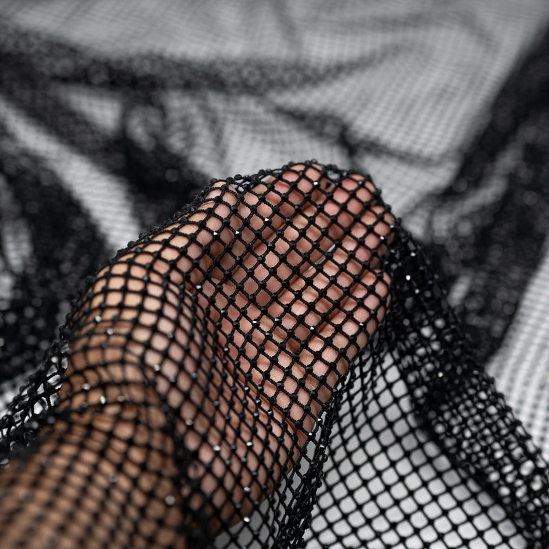 A hand pulling on a sample of Enigma Diamond Fishnet in the color Black