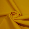 A swirled piece of matte nylon spandex fabric in the color sunset blvd yellow.