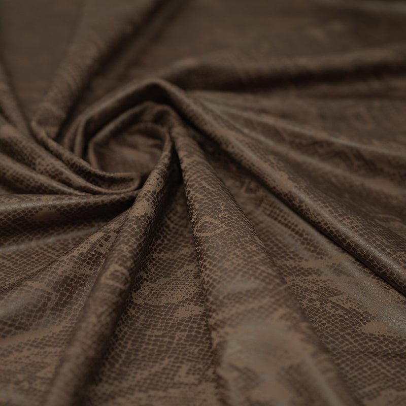 A swirled piece of Medusa Snake Skin Foil Printed Spandex in the color Brown