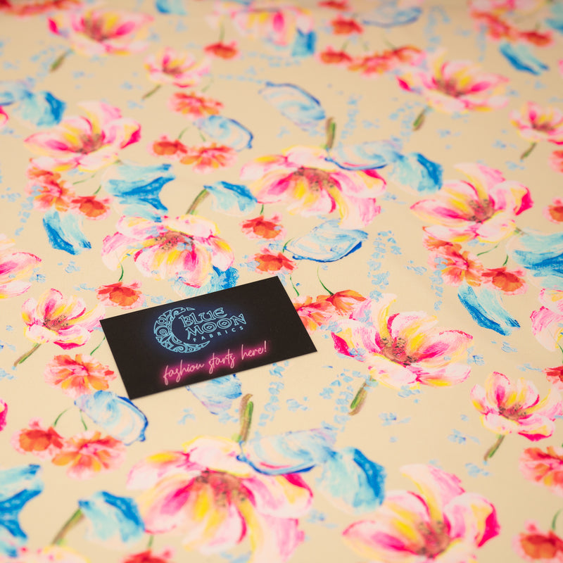 A flat sample of Painterly Flowers Printed Spandex with a Blue Moon Fabrics standard size business card laid on top of the print for pattern sizing.