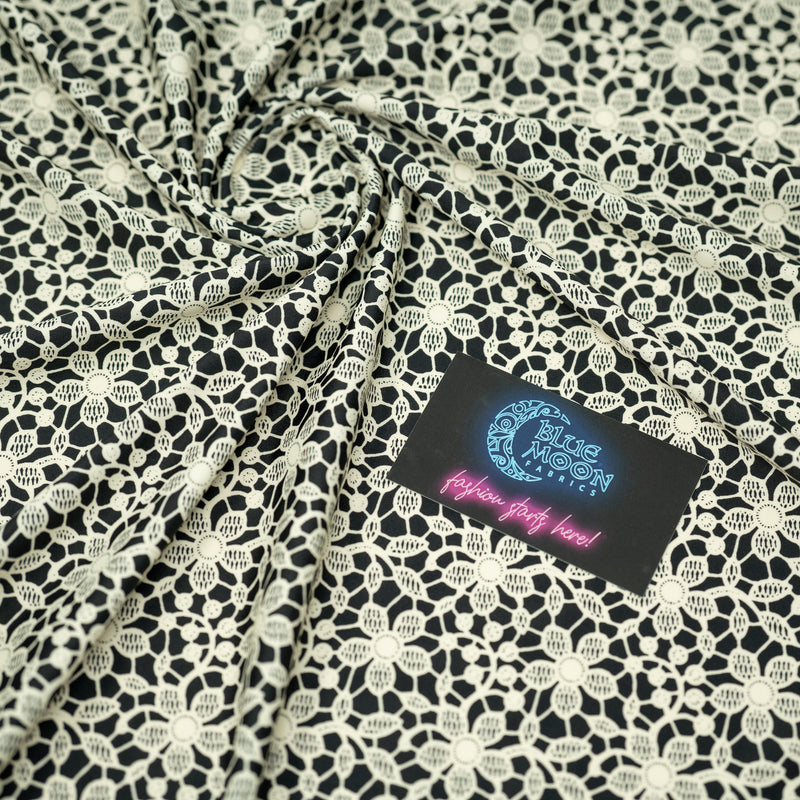 Swirled sample shot of vory Flower Lace Pattern on Black Printed Spandex with a Blue Moon Fabrics standard size business card laid on top of the print for pattern sizing.
