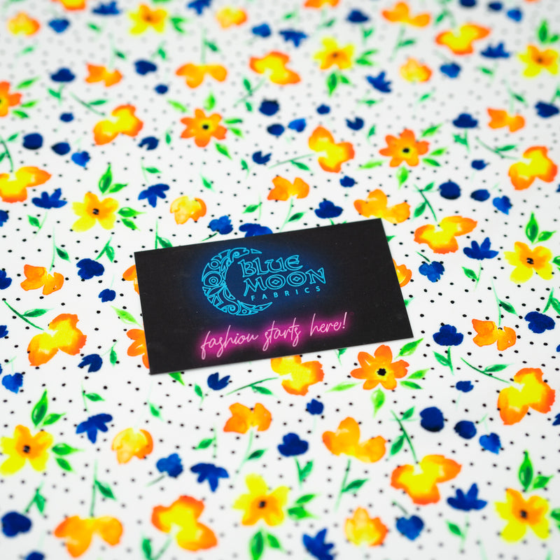A flat sample of Watercolor Flowers and Black Dots Printed Spandex with a Blue Moon Fabrics standard size business card laid on top of the print for pattern sizing.