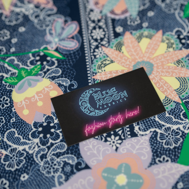 A flat sample of Chantilly Floral Lace Printed Spandex with a Blue Moon Fabrics standard size business card laid on top of the print for pattern sizing.