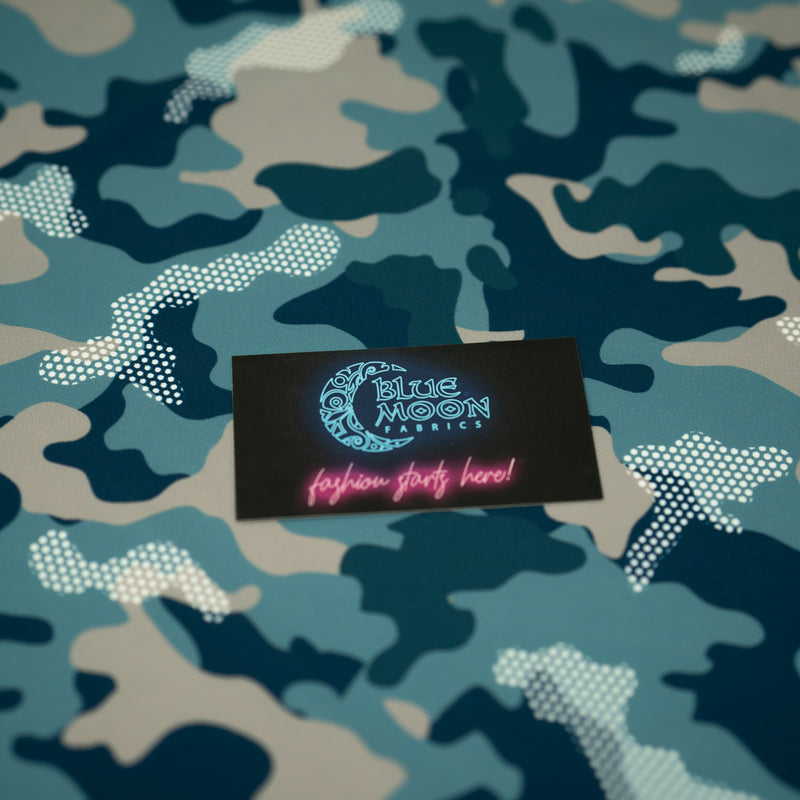 A flat sample of Fiji Camouflage Printed Spandex in the color navy-blue-white-brown with a Blue Moon Fabrics standard size business card laid on top of the print for pattern sizing.