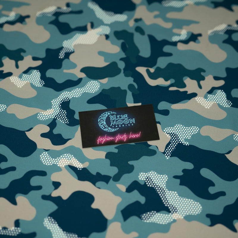 A flat sample of Fiji Camouflage Printed Spandex in the color navy-blue-white-brown with a Blue Moon Fabrics standard size business card laid on top of the print for pattern sizing.
