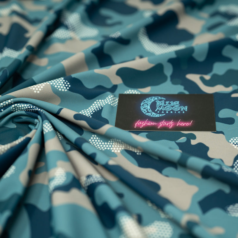 Swirled sample shot of Fiji Camouflage Printed Spandex in the color navy-blue-white-brown with a Blue Moon Fabrics standard size business card laid on top of the print for pattern sizing.