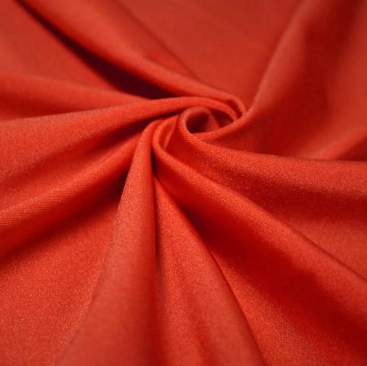 A swirled piece of shiny nylon spandex in the color hot coral.
