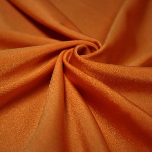 A swirled piece of shiny nylon spandex in the color penny.