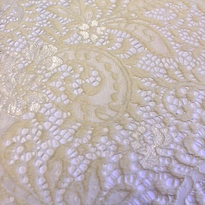 A flat sample of paige stretch lace in the color off white.