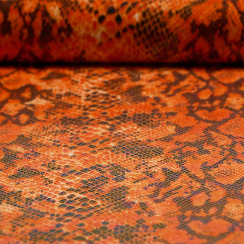 A folded sample of rattlesnake foil printed spandex in the color orange.