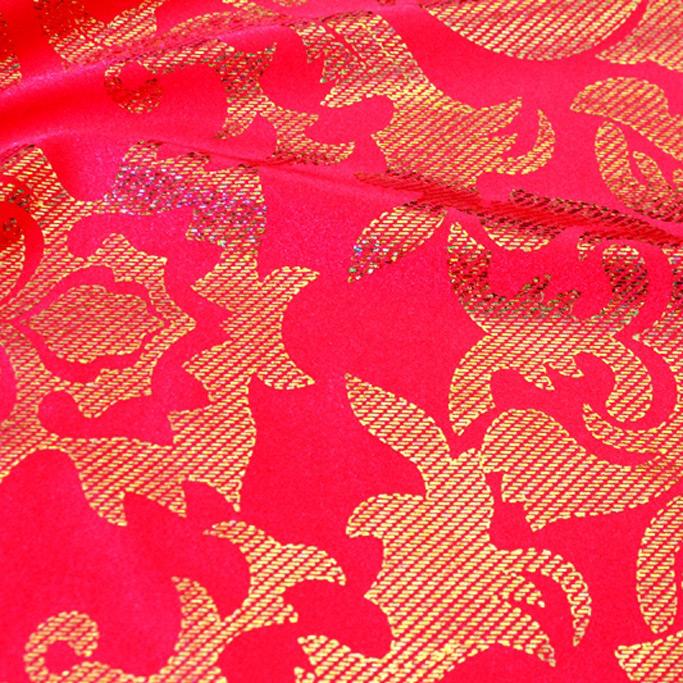 A swirled sample of rome foil printed spandex in the color watermelon red-gold.