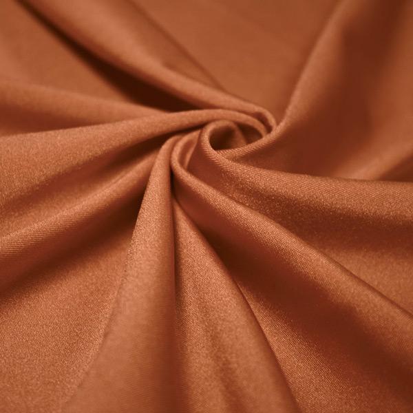 A swirled piece of shiny nylon spandex in the color bronze.
