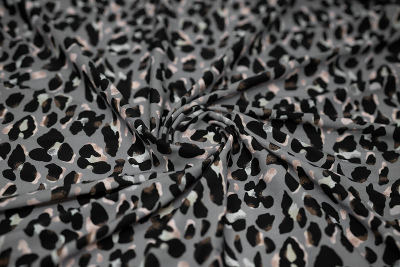 Swirled sample shot of Sporty Leopard Printed Spandex Fabric. The print is of black leopard spots with light dust brown accents and light colored shadows on a gray background.