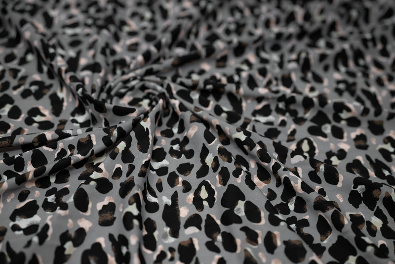 Swirled sample shot of Sporty Leopard Printed Spandex Fabric. The print is of black leopard spots with light dust brown accents and light colored shadows on a gray background.