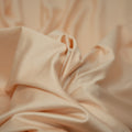 A swirled piece of nylon spandex fabric with an all over shiny look in the color Soft-Apricot