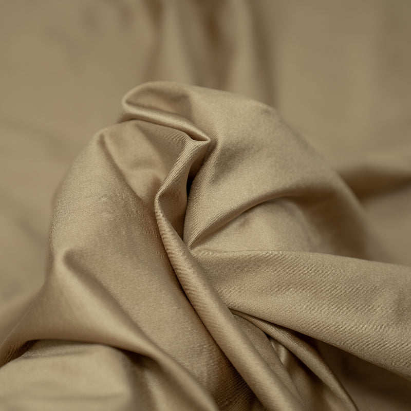 A swirled piece of nylon spandex fabric with an all over shiny look in the color taupe